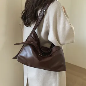 Detail of a large vintage brown shoulder bag showing eyelet strap and leather texture