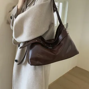 Side view of a vintage dark brown tote bag with metal eyelets worn on light coat