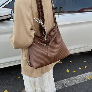 Detail of dark brown tote bag featuring vertical pleated texture and silver metal eyelets