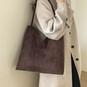 Détail du grand sac cabas en daim marron avec couture verticale sur manteau en laine
