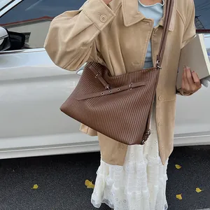 Detail of brown pleated shoulder bag with metallic eyelets and strap on street style model