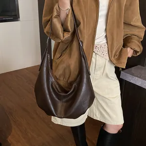 Photo du sac hobo demi-lune marron foncé avec large bandoulière porté par un modèle