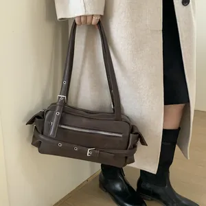 Detail of dark brown baguette bag with silver zippers and metal buckle straps on model
