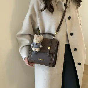 Sac bandoulière en cuir marron avec rabat léopard et pendentif ours porté par mannequin