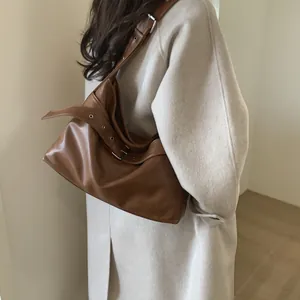 Brown leather tote bag styled with white coat showing adjustable strap and large capacity