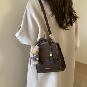 Détail du sac à main marron foncé avec motif léopard, logo doré et charm d'ours peluche