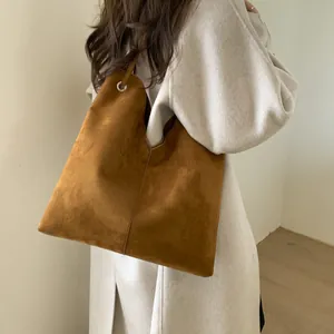 Détail du grand sac cabas en daim marron porté avec un manteau beige sur l'épaule