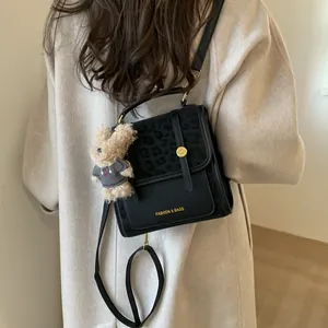 Détail du sac à dos léopard noir avec boucle dorée et breloque en forme d'ours en peluche