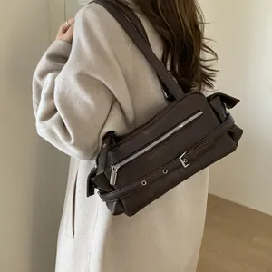 Side view of dark brown leather underarm bag worn with cream coat for styling