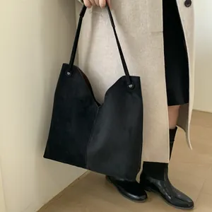 Détail d'un grand cabas noir mat avec coupe en V et fine bandoulière sur l'épaule