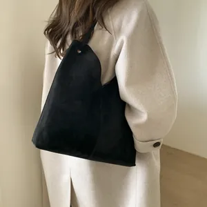 Gros plan d'un cabas en daim noir mat porté avec un manteau en cachemire beige élégant