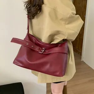 Detail of burgundy leather tote bag with large decorative buckle on minimalist background