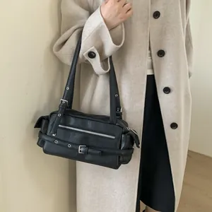 Close-up of vintage black Y2K shoulder bag with silver eyelets and buckles on beige coat