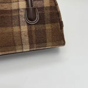 Gros plan sur le tissu à carreaux en peluche marron et la poignée en cuir de ce sac