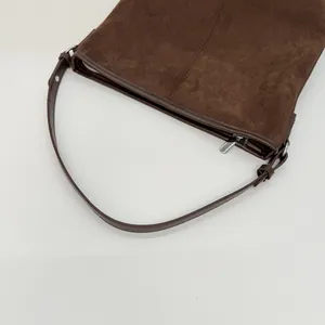 Detailaufnahme von dunkelbraunem Wildlederstoff und Lederriemen mit Metallreißverschluss