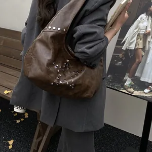Brown faux leather hobo bag with star-shaped rivet studs shown on model's shoulder