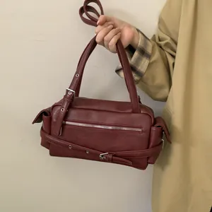 Detail of burgundy leather vintage biker style handbag with silver zippers and buckle straps