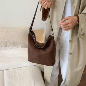 Detailansicht der dunkelbraunen Hobo-Tasche aus Wildleder an der Schulter mit Trenchcoat