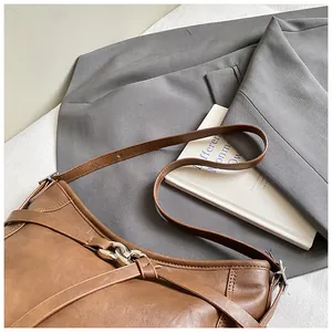 Détail d'un sac cabas en cuir marron vintage avec boucles argent sur blazer gris