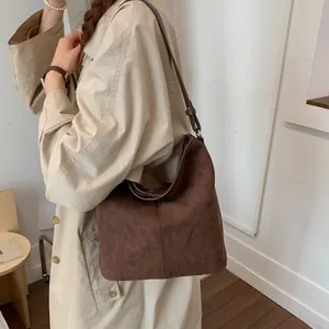 Detail der dunkelbraunen Wildleder-Eimertasche mit Ziernähten an einem Trenchcoat-Modell