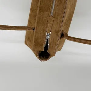 Détail d'un grand sac cabas en daim marron foncé avec fermeture éclair argentée et fines anses