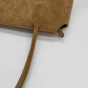 Détail de la matière en daim marron mat et des coutures sur un grand sac cabas porté épaule