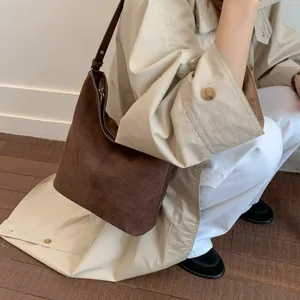 Detail der dunkelbraunen Wildleder-Beuteltasche mit Lederriemen und beigem Trenchcoat