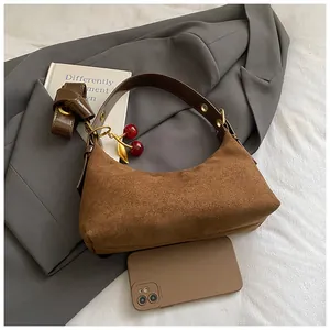 Détail sac bandoulière en daim marron avec sangle en cuir à œillets dorés et pendentif cerise