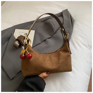 Détail du sac en daim marron avec breloque cerise posé sur une veste grise