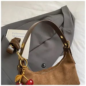 Détail du sac hobo en daim marron avec bandoulière réglable et breloque cerise vintage