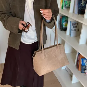 Détail du sac à bandoulière en daim mat marron clair avec longue sangle devant une étagère