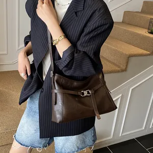 Détail d'un sac à bandoulière en cuir brillant marron foncé porté par un mannequin