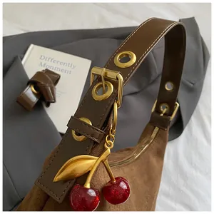 Détail d'un sac rétro marron mat avec breloque cerise et bandoulière à boucle métallique
