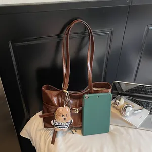 Détail d'un sac cabas marron brillant en cuir avec breloque ours sur un lit blanc épuré