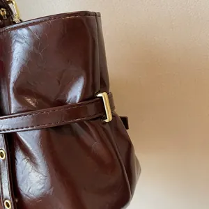 Gros plan sur le cuir huilé marron foncé et le fermoir en métal doré du sac fourre-tout