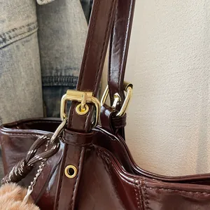 Détail du sac bandoulière en cuir bordeaux brillant avec boucle dorée et pompon