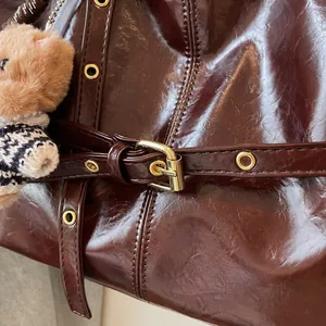 Détail du sac à main marron brillant avec boucles dorées et porte-clé ours en peluche