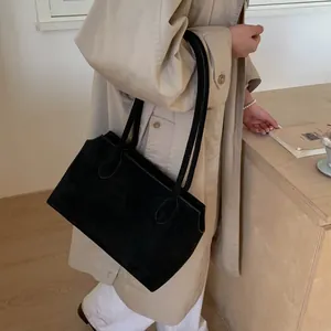 Détail d'un grand sac fourre-tout noir mat en suède porté avec un trench-coat beige élégant