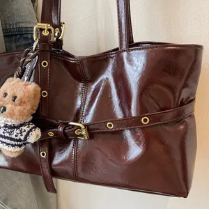 Gros plan sur la texture du cuir ciré marron foncé et la boucle dorée du sac à main