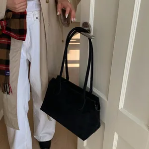 Détail d'un grand sac cabas en daim noir mat suspendu à une poignée de porte de bureau