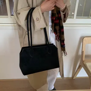 Gros plan du sac cabas en daim noir mat porté sur un trench-coat beige élégant