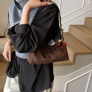 Détail d'un sac cabas marron vintage en daim avec pendentif cerise rouge et finitions métal