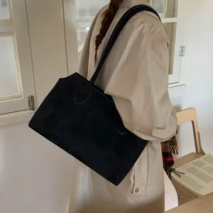Grand sac cabas noir mat porté avec un trench-coat dans un décor intérieur épuré