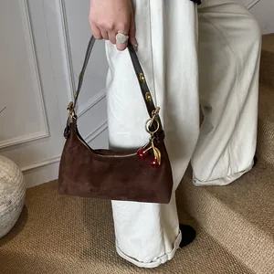 Détail du sac à bandoulière en daim marron foncé vintage avec breloque cerise rouge