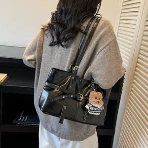 Détail du sac à bandoulière noir brillant avec boucle dorée et breloque ours mignon
