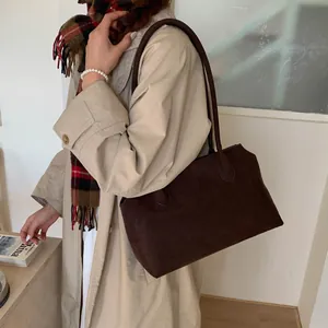 Modèle portant un grand sac cabas marron foncé en daim mat pour les tenues d'hiver