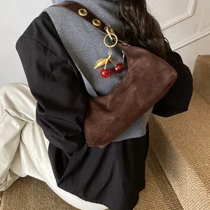 Détail du sac bandoulière en daim marron avec breloque cerise et œillets sur la sangle