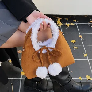 Detail of caramel suede handbag featuring white faux fur trim and fluffy pompom charms