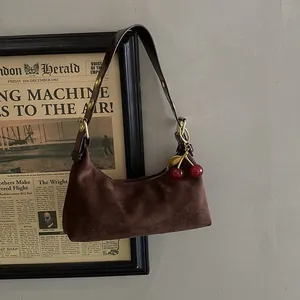 Détail du sac à bandoulière en daim marron avec breloque cerise et lanière en cuir à anneaux