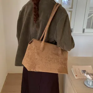 Détail du sac fourre-tout en daim marron porté à l'épaule pour un style vintage minimaliste